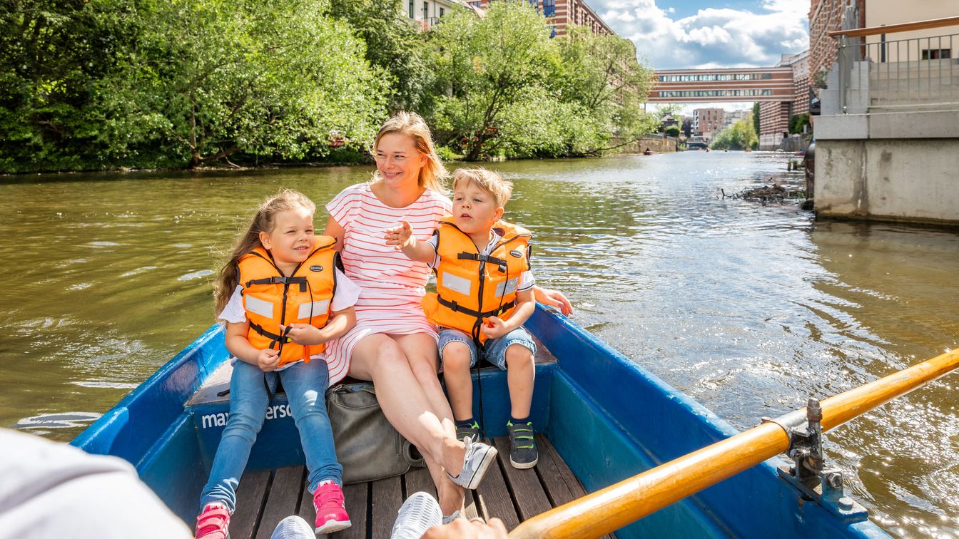 Eine Mutter sitzt mit ihren Kindern in einem Boot, das über die Wasserwege in Leipzig rudert. 