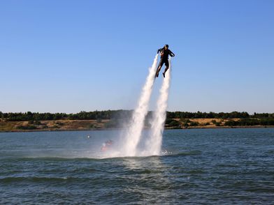 Jetlev-Fly am Störmthaler See, zu sehen ist eine Person, die eine Art Raketenrucksack trägt, der die Person mittels eines Rückstoßantriebs mit Wasserstrahlen über der Wasseroberfläche bewegt © Andreas Schmidt