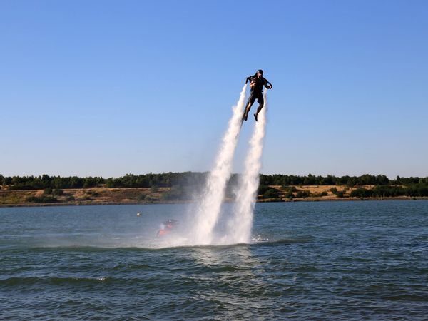 Jetlev-Fly am Störmthaler See, zu sehen ist eine Person, die eine Art Raketenrucksack trägt, der die Person mittels eines Rückstoßantriebs mit Wasserstrahlen über der Wasseroberfläche bewegt © Andreas Schmidt