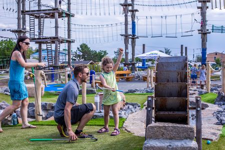 Das Bild zeigt eine junge Familie beim Mini-Golf Spielen. Der Vater hilft seiner Tochter beim Zielen. 