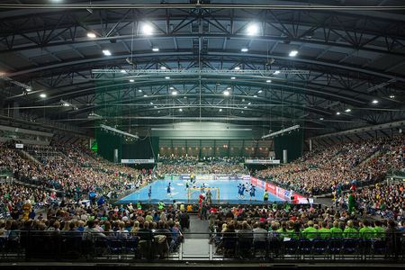 Zwei Mannschaften spielen in der Arena Leipzig Handball gegeneinander. Die Zuschauerränge sind mit Publikum gefüllt.