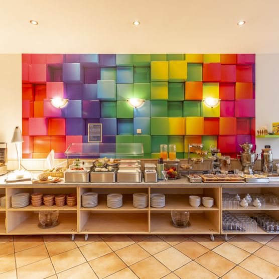 Das Bild zeigt das reichhaltige Frühstücksbuffet vor einem bunten Gemählde.
