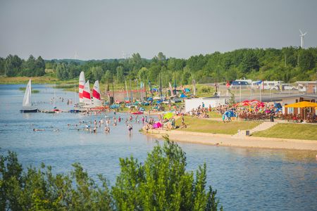 Das Bild zeigt die resorteigene Bucht am Schladitzer See mit Sandstrand, Volleyballfeldern und Kite-Surfern.