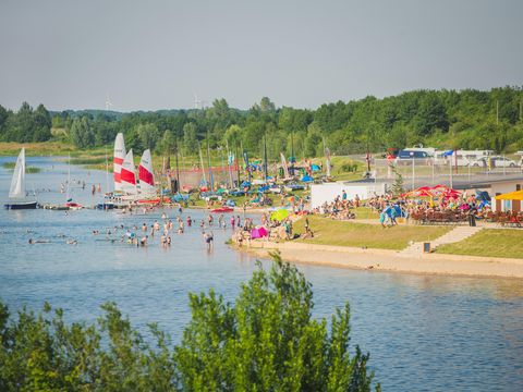 Das Bild zeigt die resorteigene Bucht am Schladitzer See mit Sandstrand, Volleyballfeldern und Kite-Surfern.