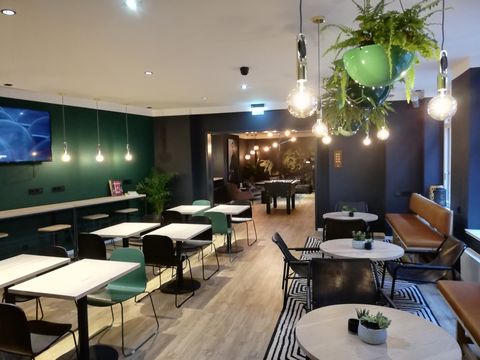 Moderner Aufenthaltsraum ausgestattet mit Tischen und Stühlen, einem Kickertisch und einem Lounge-Bereich.