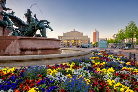 Mendebrunnen auf dem Augustusplatz in Leipzig mit Blumen im Frühling, dahinter die Oper Leipzig