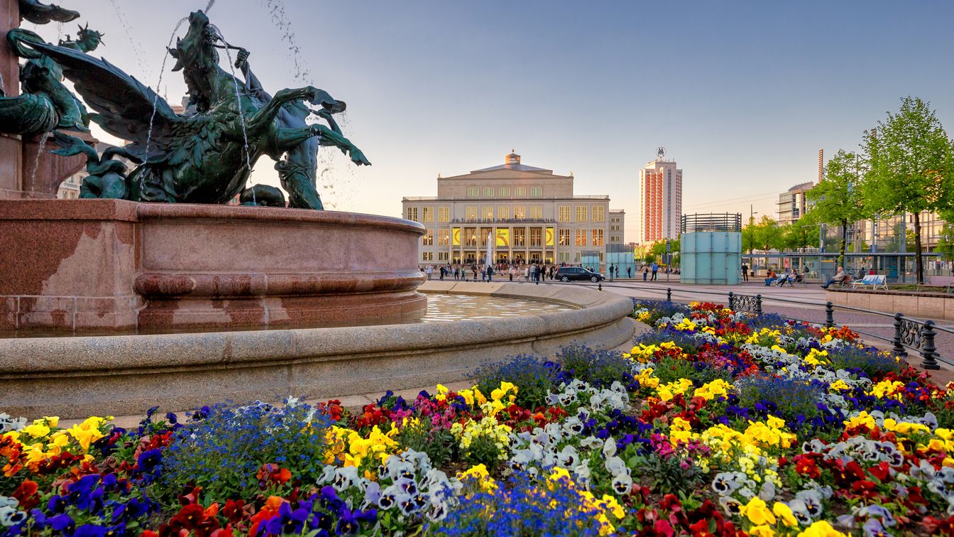 Mendebrunnen auf dem Augustusplatz in Leipzig mit Blumen im Frühling, dahinter die Oper Leipzig