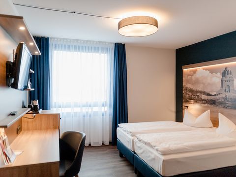 Das Bild gibt Einblick in ein komfortables Doppelzimmer des Atlanta Hotel Leipzig, mit Schreibtisch und TV. 