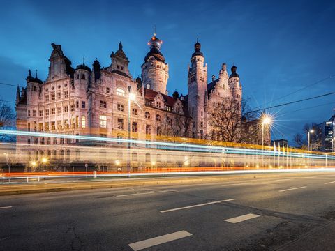 Blick auf das beleuchtete Neue Rathaus in Leipzig. Im Vordergrund sieht man nur die Lichtspuren einer vorbeifahrenden Tram.