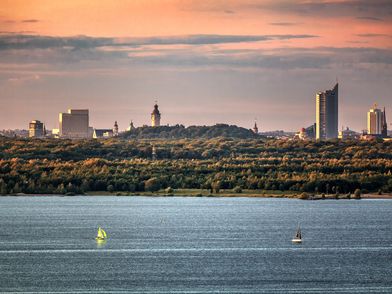 Das Bild zeigt den Cospudener See mit der Leipziger Skyline im Hintergrund.