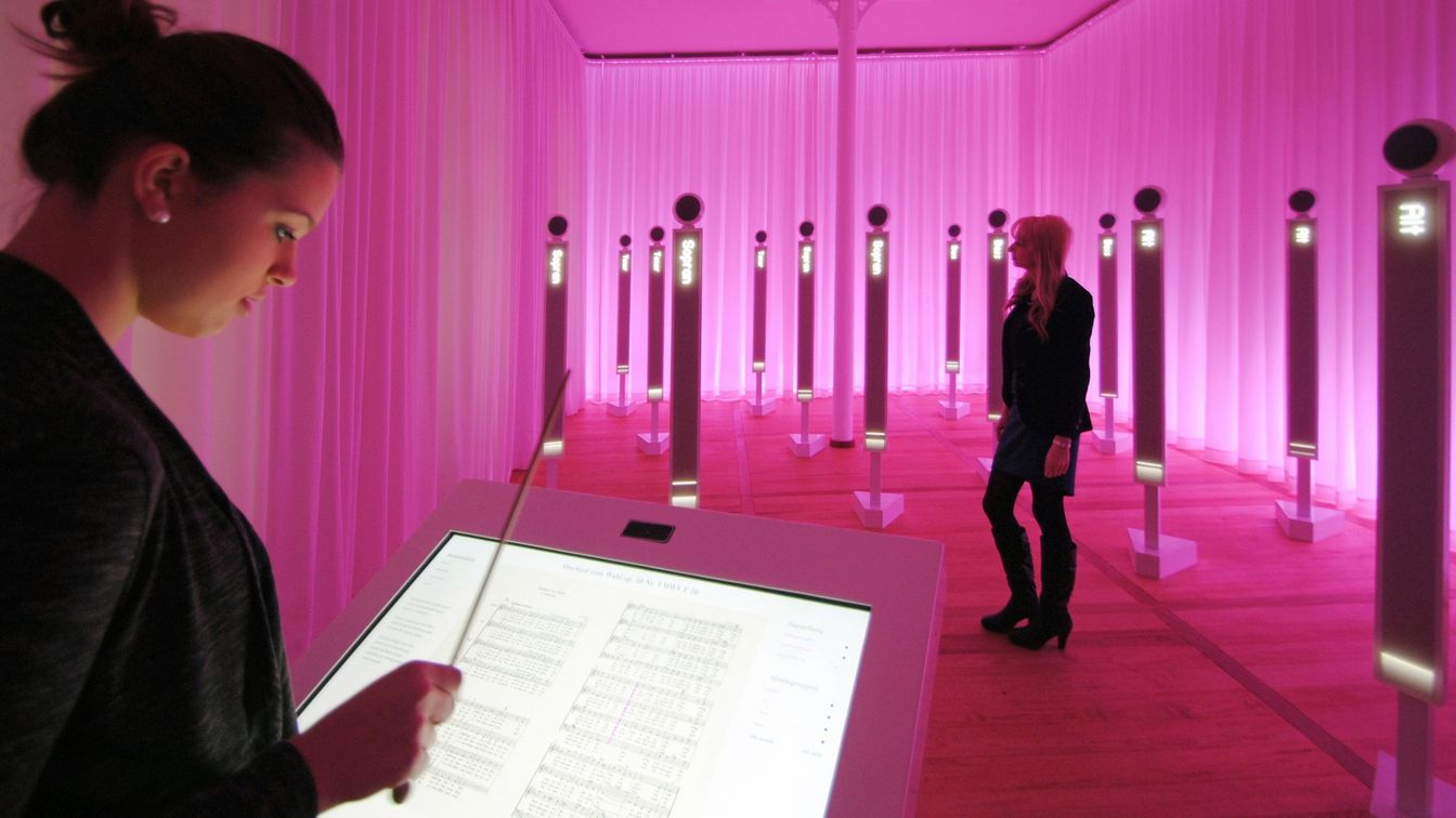 Das Bild zeigt das Effektorium im Erdgeschoss des Mendelssohn-Hauses Leipzig mit einem Dirigentenpult und Stelen. Hier kann man ein virtuelles Orchester bzw. einen Chor dirigieren.