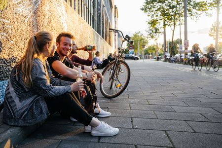 Drei junge Menschen sitzen entspannt mit Getränken in der Hand am Westwerk auf der Karl-Heine-Straße im Leipziger Szeneviertel Plagwitz