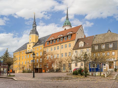 Das Bild zeigt die gelbe Fassade des Roßweiner Rathaus, dahinter sieht man die Stadtkirche. 