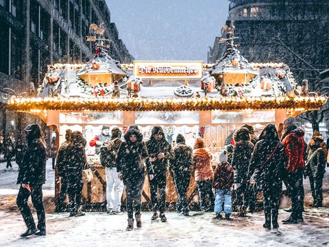 Gdy śnieg pada obficie, goście Rynku Bożonarodzeniowego w Lipsku stojący przed straganami chowają głowy w kapturach