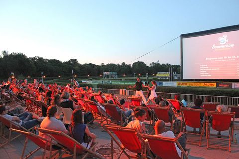 Auf der Pferderennbahn sitzen die Besucher in roten Liegestühlen vor einer großen Leinwand, Open Air Kino in Leipzig, Sommer