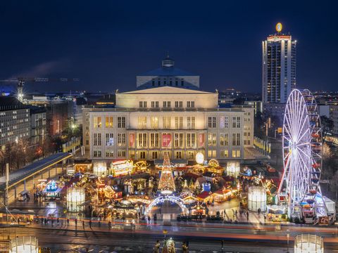 Pohled z budovy Gewandhausu na vánoční trhy na Augustusplatzu v centru Lipska s budovou opery a mrakodrapem Wintergarten v pozadí