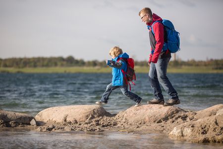 Das Bild zeigt Vater und Sohn wie sie auf den großen Steinen am See balancieren.