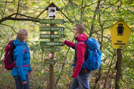 Ein Paar macht eine Wanderung und schaut sich den Wegweiser im Wald zur Orientierung an. 