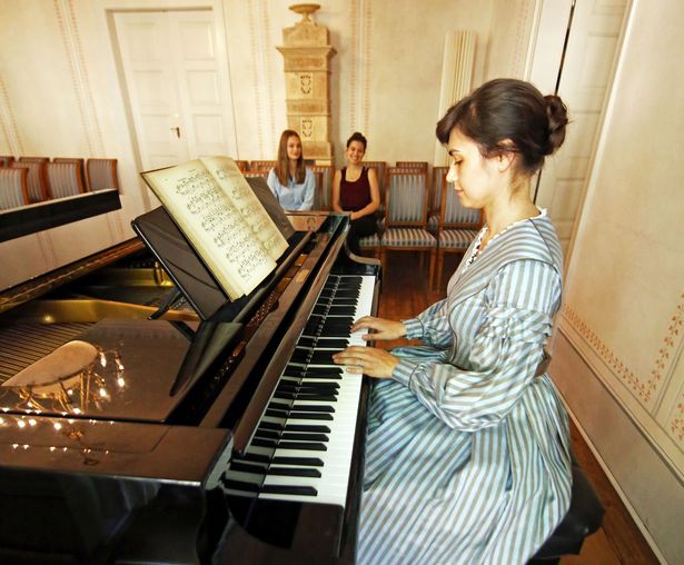 Une jeune femme représente la compositrice originaire de Leipzig Clara Schumann au piano dans le salon historique de la Maison-musée Schumann, tandis que deux jeunes auditrices la regardent avec admiration pendant son concert.