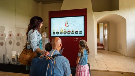 Eine vierköpfige Familie schaut sich über einen Infoscreen die Ausstellung der Burg Mildenstein an.
