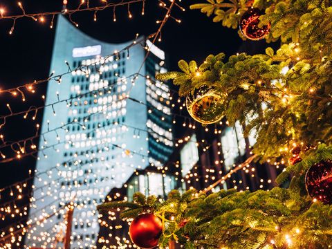V centru pozornosti je ozdobená jedle a světelné řetězce na vánočních trzích na lipském Augustusplatzu, v pozadí se tyčí městský mrakodrap 