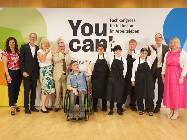 Eine Gruppe von Personen bei der Pressekonferenz zum Fachkongress ‚You can! 2026‘ zeigt gemeinsam auf die Logowand im Hintergrund für Tagung & Konferenz Leipzig Convention