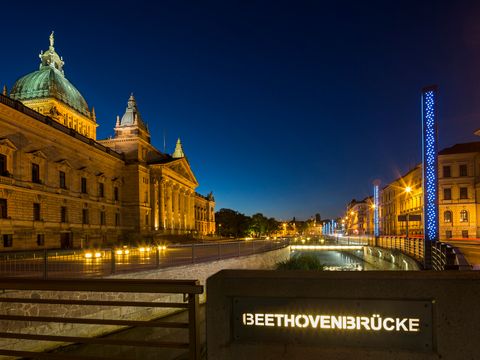 Das Bild zeigt die erleuchtete Fassade des Bundesverwaltungsgericht und die Beethovenbrücke über dem Pleißemühlgraben. 