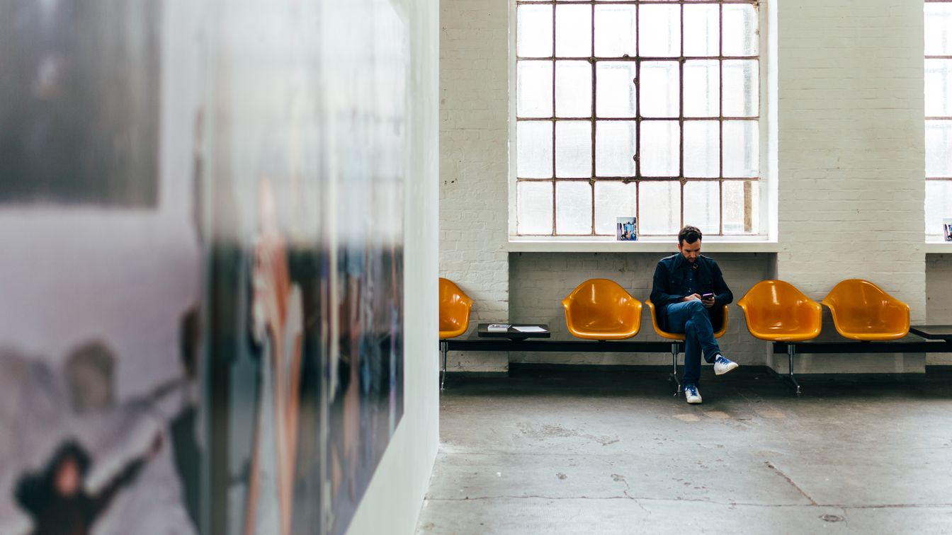 Foto von einem Ausstellungsraum im Kunstzentrum Spinnerei in der ehemaligen Baumwollspinnerei Leipzig in Plagwitz, auf der linken Seite ist ein ausgestelltes Gemälde zu sehen, dem Blickwinkel gegenüber sitzt eine Person auf einer Bank unter den großen Fenstern des Industriegebäudes