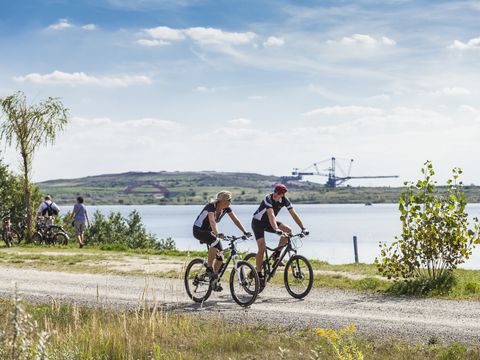 zwei Fahrradfahrer vor dem Hintergrund des Markkleeberger Sees und des Bergbau-Technik-Parks