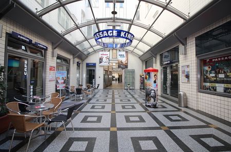 Blick in die Passage mit dem gefliesten Boden, den Fenstern an der Decke und dem Eingang zum Kino auf der rechten Seite.
