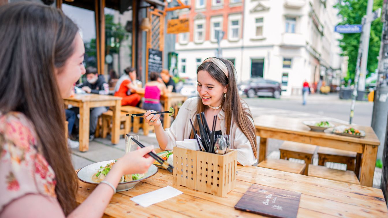 Zwei Freundinnen sitzen im Außenbereich des Com Nieu und genießen in freudiger Stimmung ihr Essen