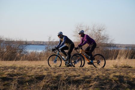Zwei Männer fahren Gravelbike, im Hintergrund ist ein See zu sehen, Region Leipzig
