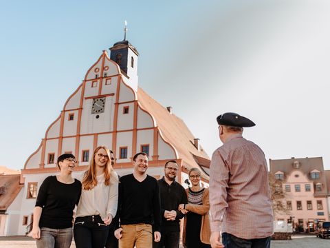 Eine Gruppe Touristen und ein Stadtführer mit Kochhaube vor dem Grimmaer Rathaus.