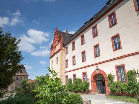 Das Bild zeigt die gelbe Fassade des Schlosses mit den markanten roten Gieblen und dem imposanten Tor.