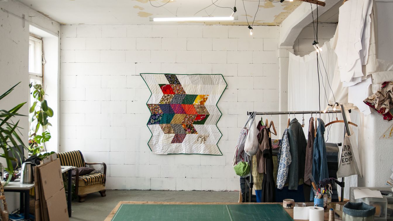 Das Bild zeigt das Atelier mit Materialien und einem Quilt.
