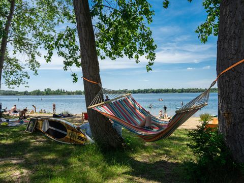 A hammock between two trees at Lake Kulkwitz. Relaxation, sunshine, water sports, sandy beach, clear water.