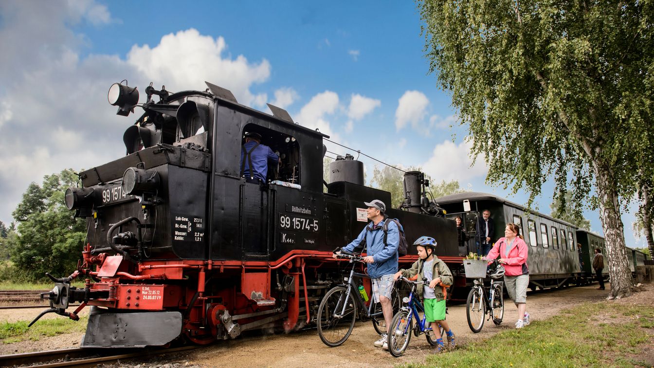Eine Familie steht mit ihren Fahrrädern an einem sommerlichen Tag vor einer Dampfeisenbahn in der Leipzig Region.