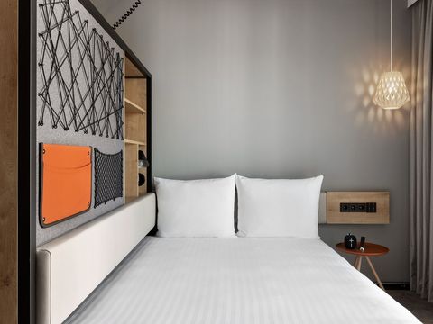 Links angrenzend an das Doppelbett befindet sich ein moderner Raumtrenner mit Stauraum aus Holz