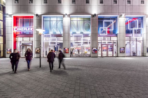 Kinobesucher gehen in das hell ausgeleuchtete Gebäude des Cineplex Leipzig, Kinos in Leipzig, Freizeit 