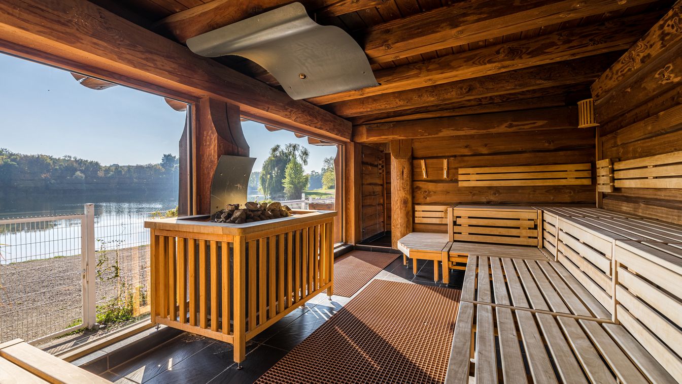 Das Bild zeigt den Innenraum einer Sauna mit Panoramafenster auf einen idyllischen See.