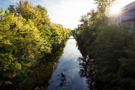 Das Bild zeigt ein Kanu auf dem Karl-Heine Kanal, der links und rechts von grünen Bäumen und Sträuchern umgeben ist.