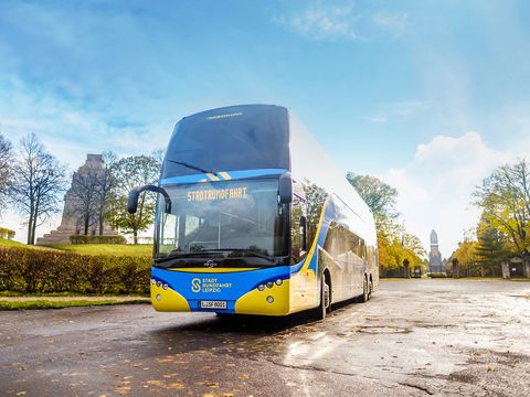 Ein blau-gelber Bus von Stadtrundfahrt Leipzig GmbH steht bei einer Bustour vor dem Völkerschlachtdenkmal