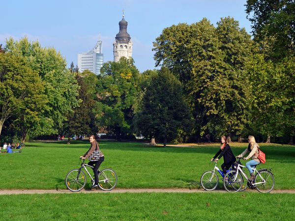 Fahrradtour im Johannapark, zu sehen sind drei junge Frauen auf ihren Fahrrädern im Johannapark, im Hintergrund sieht man den Rathausturm des Neuen Rathauses und das City-Hochhaus © Andreas Schmidt