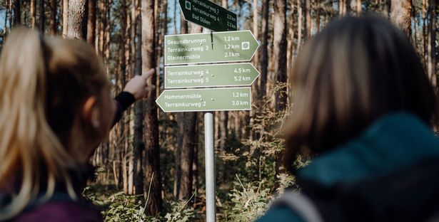 Zwei Menschen erkundigen sich nach einer Wanderroute an einem Wegweiser im Wald, Wandern in der Region, Aktiv 