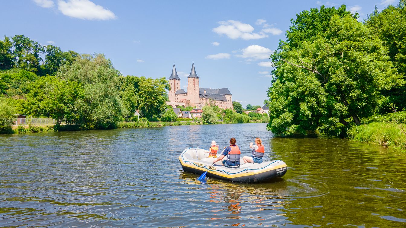 Eine Familie paddelt auf der Mulde in einem Schlauchboot in Richtung Schloss Rochlitz.
