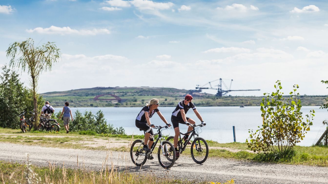 Zwei Fahrradfahrer vor dem Hintergrund des Markkleeberger Sees und des Bergbau-Technik-Parks