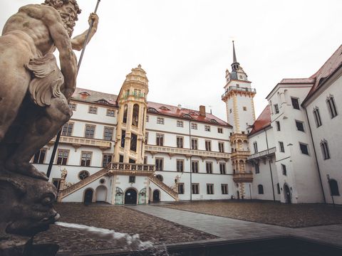 Blick auf den Innenhof von Schloss Hartenfels in Torgau, der Region Leipzig, welches im Stil der Frührenaissance gebaut wurde, links im Bild in eine Statue aus Stein zu sehen, der Innenhof ist in den Farben gold, rot und braun gehalten