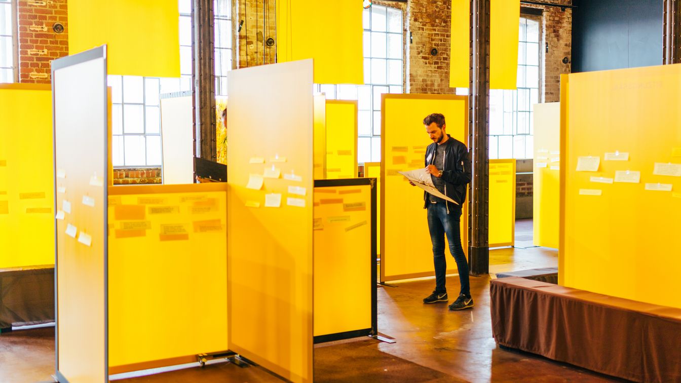 Ein Raum im Spinnerei Kunstzentrum in der ehemaligen Baumwollspinnerei in Leipzig Plagwitz, der mit mehreren gelben Plexiglastrennwänden befüllt ist, die zusammen ein Kunstwerk darstellen. Im hinteren rechten Bereich des Raumes steht ein interessierter Mann