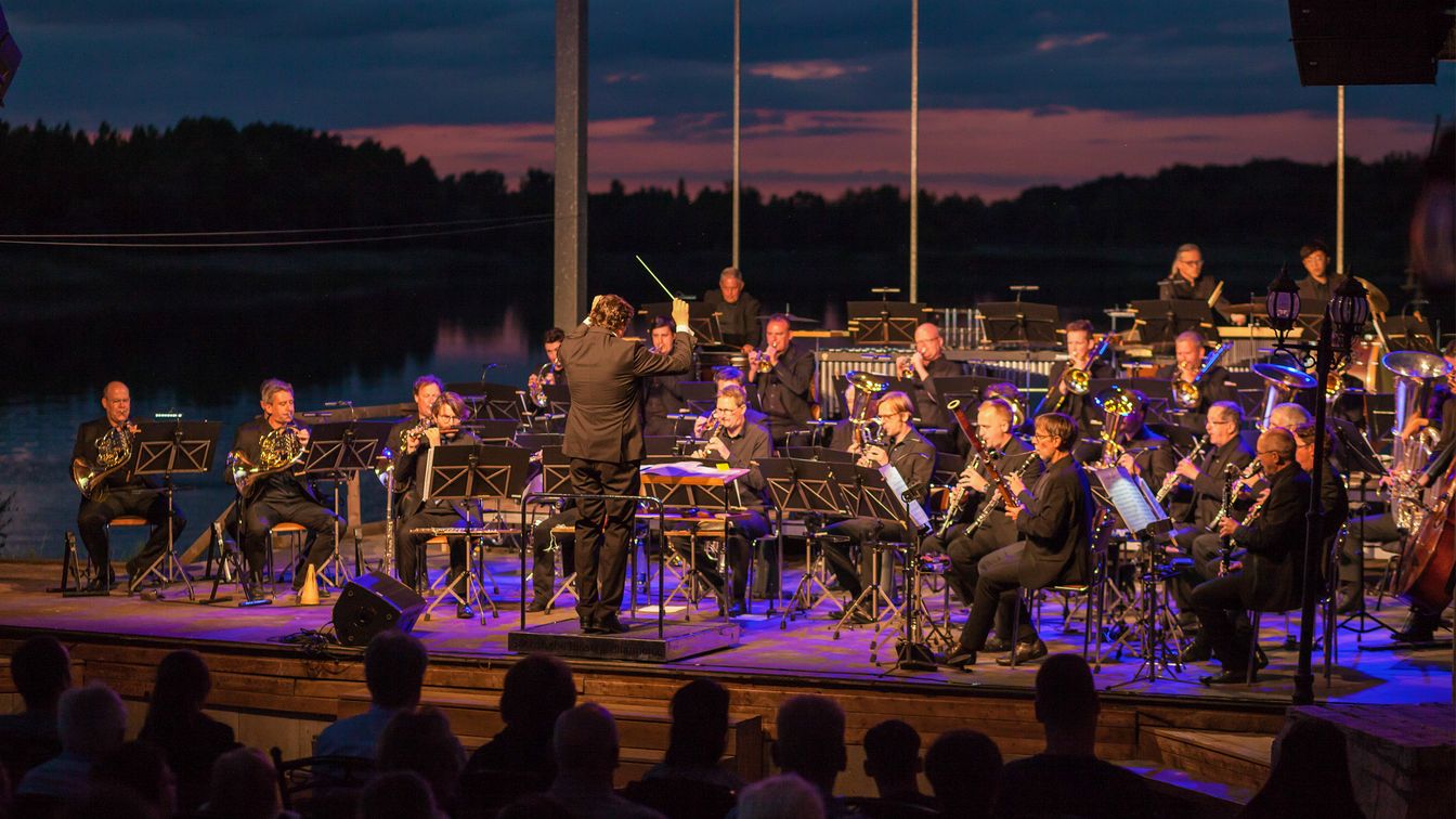 Das Orchester der Sächsischen Bläserphilharmonie spielt auf der Seebühne des Biedermeierstrands in Schkeuditz in der Region Leipzig. Im Hintergrund sieht man den Schladitzer See vor dem Nachthimmel