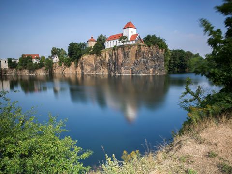 Das Bild zeigt die Bergkiche in Beucha auf einem Vorsprung trohnend über dem kleinen Tagebau-See.